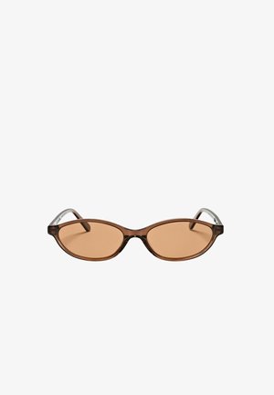 Lunettes de soleil ovales marron avec des montures étroites et des verres marron légèrement teintés, présentées sur un fond blanc uni.