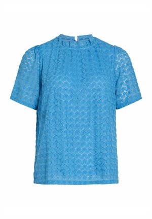 Blouse texturée bleue à manches courtes, avec un col rond et une ouverture clé au dos. Le tissu présente un motif en nid d'abeille et un léger éclat.