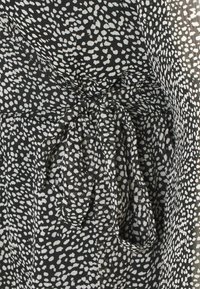 Czarnobiała tkanina w kropki o teksturowanej powierzchni, z wiązanym detalem w talii i zwiewnym krojem.