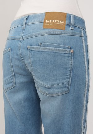 Light blue denim jeans featuring a leather tag reading "GANG," five pockets, a distressed hem, and a slim fit design.
