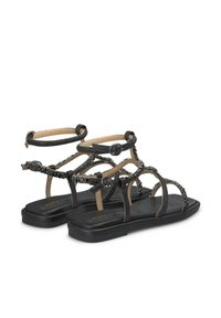Zwarte platte sandalen met meerdere bandjes, voorzien van decoratieve kralenaccenten en verstelbare enkelriemen, geplaatst op een platte zool.