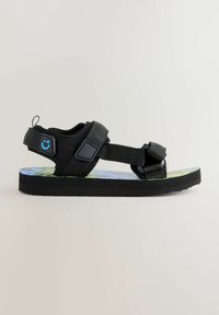 Svart sandal med flera justerbara remmar, en strukturerad sula och en färgglad mönstrad fotbädd med blå och gröna mönster.