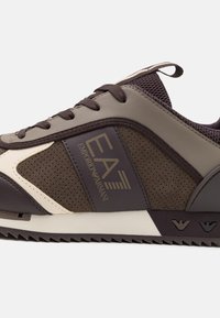 Sneaker in pelle marrone e rete con superficie testurizzata, accenti beige a contrasto e un logo. Suola in gomma con motivo a zigzag.