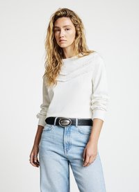 Weißes Sweatshirt mit strukturierten horizontalen Streifen auf der Brust, kombiniert mit hellblauen Jeans und schwarzem Gürtel.