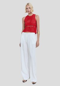 Red crochet cropped tank top with circular pattern detail, paired with high-waisted white wide-leg trousers and black sandals.