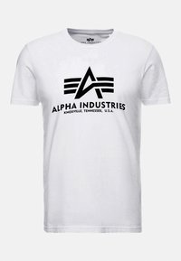 Bílý bavlněný tričko s černým logem s trojúhelníkovým designem a textem "ALPHA INDUSTRIES KNOXVILLE, TENNESSEE, U.S.A." umístěným uprostřed na přední straně.