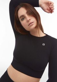 Top corto nero a maniche lunghe realizzato in tessuto liscio, con un motivo a coste sulle maniche e un piccolo logo sul petto.