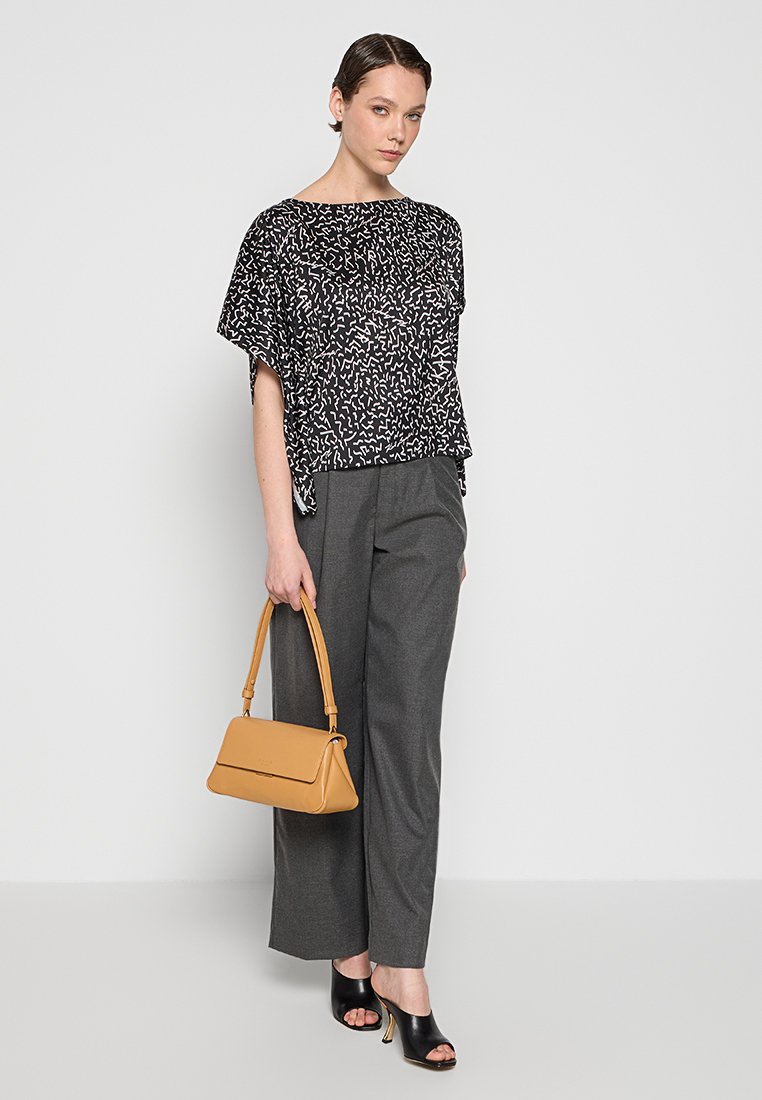 Blouse à manches courtes à motifs noir et blanc, pantalon large gris et sac à main jaune, associés à des talons ouverts noirs.