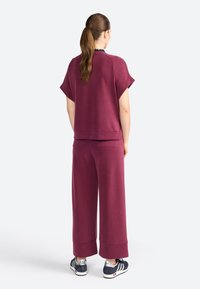 Burgunder Sweatshirt mit kurzen Ärmeln, kombiniert mit weiten Hosen aus weichem Material. Sneaker mit blau-weißen Design runden den Look ab.