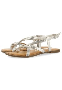 Sandalias de color plateado metálico con tiras entrelazadas, diseño de punta abierta, hebilla ajustable en el tobillo y suela plana marrón, con textura suave.