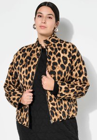 Giacca bomber con stampa leopardata, caratterizzata da un motivo nero e beige, chiusura con zip, polsini a coste e tasche laterali, abbinata a un vestito nero strutturato.