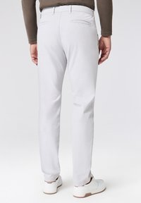 Pantaloni grigi chiari con una vestibilità slim, realizzati in tessuto liscio. Presentano due tasche posteriori e sono abbinati a sneakers bianche.