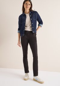 Mörk jeansjacka med två framfickor, bärs över en ljus tröja och svarta tajta byxor. Avslutas med vita sneakers med blå detaljer.