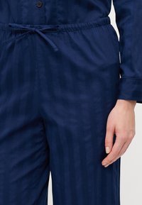 Marineblå loungewear-sett med knappegenser og bukser med snøring, med et subtilt stripemønster og myk, glatt stoffstruktur.