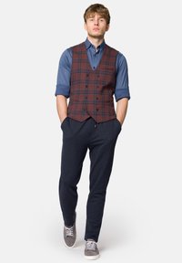Brązowa i niebieska kamizelka w kratę na niebieskiej koszuli, w połączeniu z granatowymi dresami i szarymi sneakersami. Prosty krój, casualowy design i wygodny materiał.