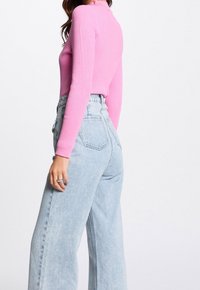 Maglietta a maniche lunghe fucsia a costine abbinata a jeans a vita alta azzurri a gamba larga, che mostrano una vestibilità rilassata e un tessuto strutturato.