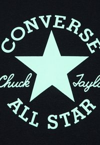 Fekete anyagon egy nagy menta zöld csillag található, amelyen a "CONVERSE", "Chuck" és "ALL STAR" szövegek vastag, fehér betűkkel olvashatóak.