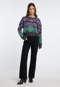 Maglione a maglia con un motivo geometrico in viola, verde acqua e nero, con un design corto e maniche lunghe, abbinato a pantaloni neri a zampa.