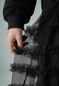 Mustmust tütel, millel on lainelised kihid. Käsi hoiab kangast, rõhutades selle läbipaistvat tekstuuri ja detailseid äärmusi.