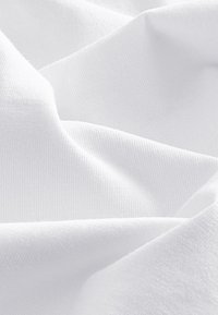 Gros plan sur un tissu blanc doux avec une texture visible et des plis délicats créant des couches lisses et superposées.