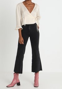 Ljusbeige omslagstopp med långa ärmar och utsvängda ärmar, kombinerad med högmidjade svarta utsvängda jeans och rosa ankelstövlar med klack.