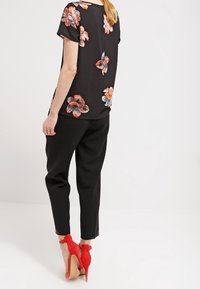 Blusa negra con flores y mangas cortas, con patrones florales rojos y azules; combinada con pantalones negros y zapatos de tacón rojos.
