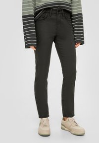 Jean vert foncé avec une coupe slim, cinq poches et passants de ceinture ; associé à des baskets beiges et un pull à rayures à manches longues.