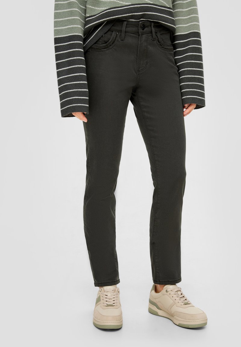 Jean vert foncé avec une coupe slim, cinq poches et passants de ceinture ; associé à des baskets beiges et un pull à rayures à manches longues.