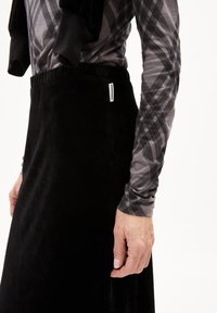 Schwarzer samtiger Rock mit glatter Textur und elastischem Bund. Langärmliges graues Shirt mit einem schwarz-weißen Karomuster.