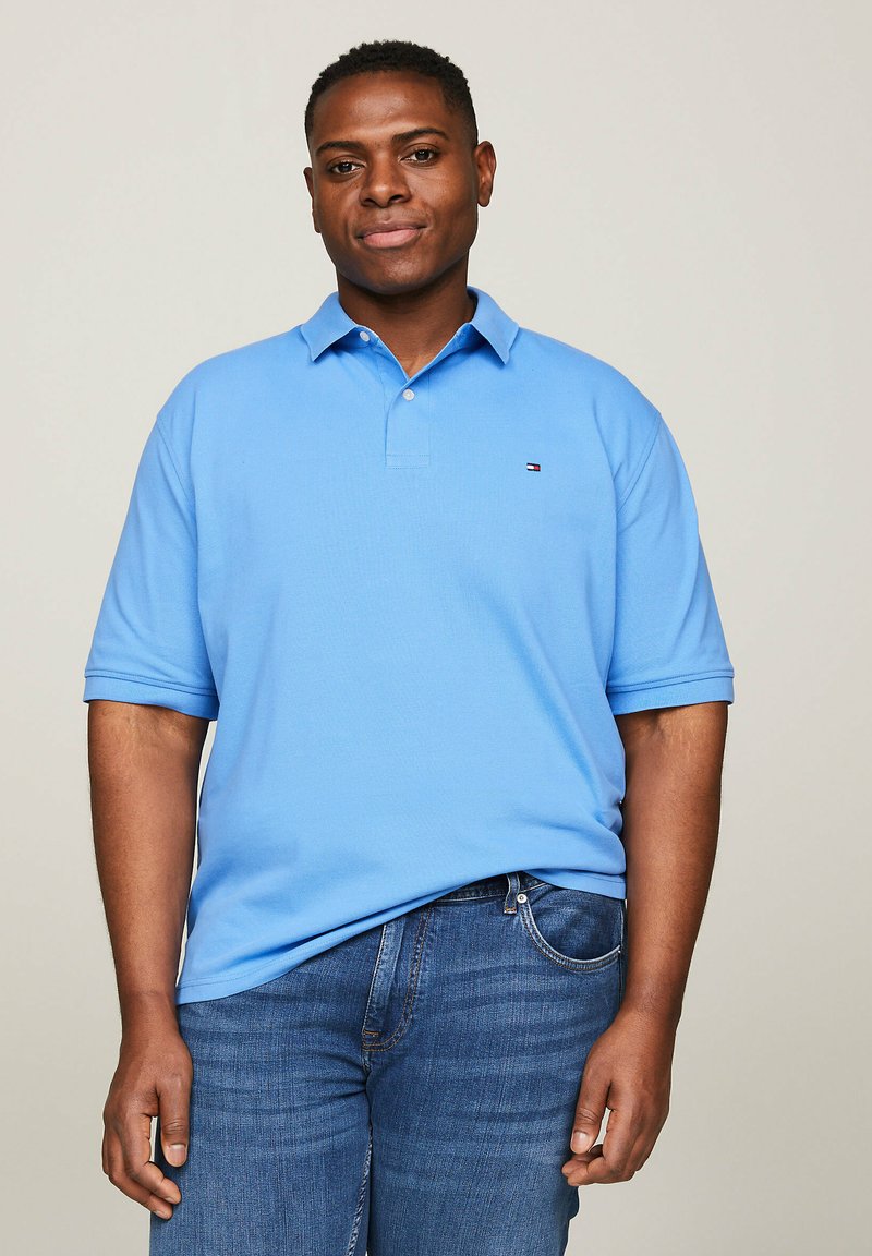 Polo shirt azzurro chiaro in cotone, dotato di colletto, maniche corte e un piccolo logo sul petto. Indossato con jeans in denim blu.