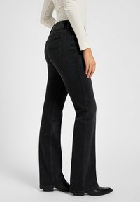 Jean noir évasé avec une texture en denim lisse, taille mi-haute et une ceinture noire embossée avec un logo. Les poches arrière présentent des détails de couture subtils.