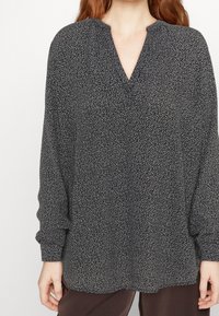 Blusa nera a maniche lunghe con scollo a V, caratterizzata da un motivo maculato bianco, in tessuto leggero, e una vestibilità leggermente ampia.