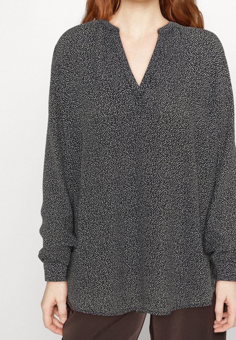Blusa nera a maniche lunghe con scollo a V, caratterizzata da un motivo maculato bianco, in tessuto leggero, e una vestibilità leggermente ampia.