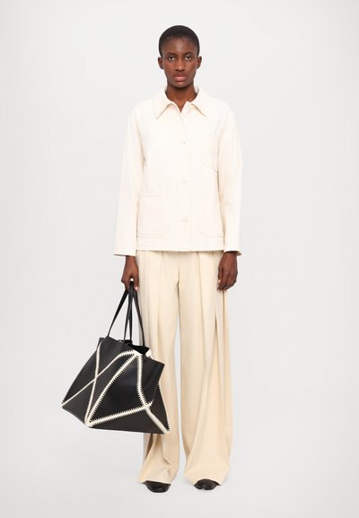Beige cotton jacket with a pointed collar, paired with cream wide-leg trousers. Black bag with white zigzag stitching, held with black straps.