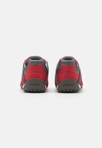 Scarpe sportive rosse e grigie con parte superiore in suede e tessuto, caratterizzate da una punta tonda e suola in gomma. Logo visibile sul tallone.