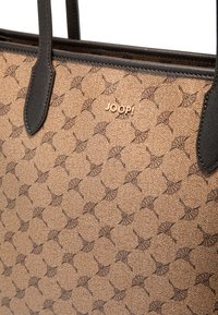 Borsa beige con superficie testurizzata caratterizzata da un motivo ripetuto. Accenti in pelle nera e logo dorato sul davanti. Due manici robusti.