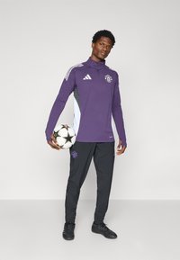 Purple long-sleeve sports top with white accents and a logo; black tapered pants with a logo; black soccer ball with star pattern.