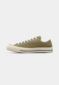 Baskets en toile vert olive avec des lacets blancs et une semelle en caoutchouc. Comprend une bande noire le long de la semelle et un design de capuchon rond.