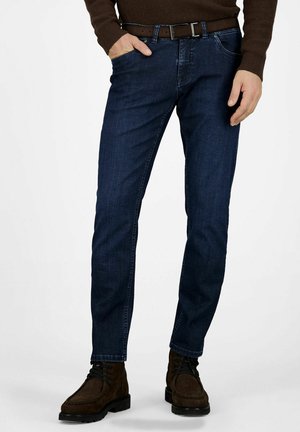 Dunkelblaue Denim-Jeans im Slim-Fit mit einem Fünf-Taschen-Design und sichtbaren Nähten, kombiniert mit braunen Schnürstiefeln.