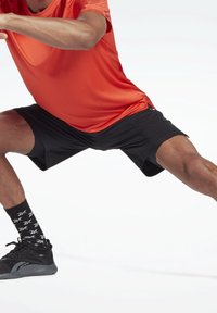 Conjunto atlético que incluye una camiseta roja que absorbe la humedad, pantalones cortos deportivos negros, zapatillas negras y calcetines negros con un patrón y acentos blancos.