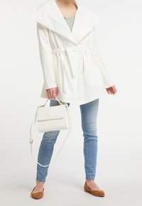 Hvid, langærmet frakke med bred krave og bindebånd i taljen, parret med lyseblå jeans og en struktureret hvid håndtaske.