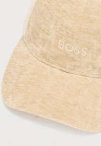 Gorra beige hecha de tela texturizada con una visera curva. "BOSS" bordado en la parte frontal en un color a juego.