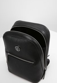 Czarny skórzany plecak z dwoma komorami na zamek błyskawiczny, przednią kieszenią na suwak oraz okrągłym logo. Gładka faktura i minimalistyczny design.