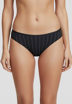 Kvinde iført sorte bikiniunderdel med tynde, lodrette hvide striber, vist fra midt på torsoen til øvre lår mod en ensfarvet baggrund.