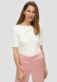 Witte top met korte mouwen en een brede halslijn, voorzien van een diagonale uitsnijding. Gecombineerd met lichtroze satijnen broek, met een gladde textuur en een getailleerde pasvorm.