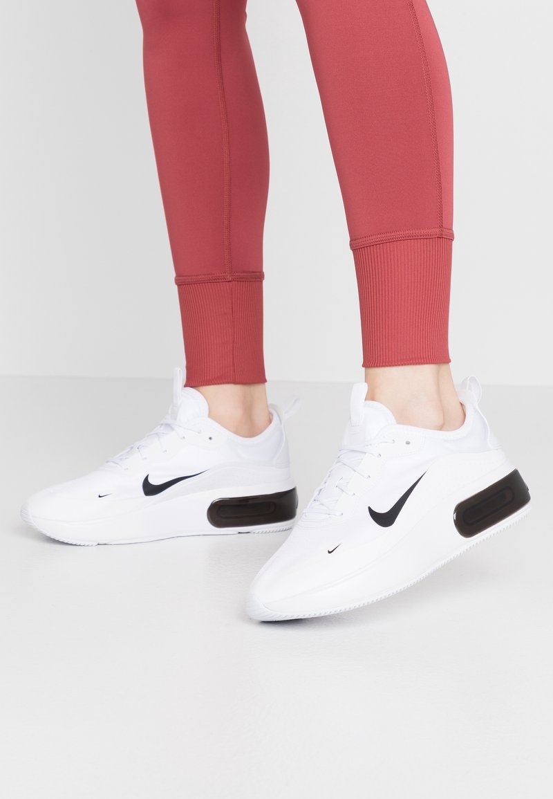Vita atletisk sneakers med en svart Nike-swoosh, med en smidig design, texturerad ovandel och en synlig luftdämpningsenhet.