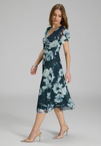 Robe midi à imprimé floral en vert foncé avec des accents bleu clair et blanc. Présente des manches bouffantes courtes et un col en V. Tissu transparent et fluide.