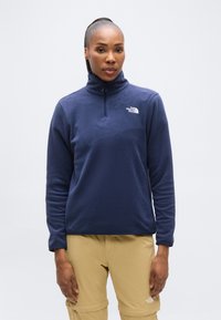 Μπλε σκούρο φλις πουλόβερ με ψηλό γιακά και φερμουάρ τετάρτου μήκους, με το λευκό λογότυπο της North Face στο αριστερό μέρος του στήθους. Λεπτή υφή, μακριά μανίκια.