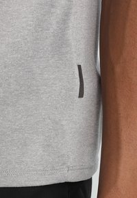 Camiseta gris de manga corta con una textura suave, que presenta una pequeña etiqueta negra en el lado. La prenda tiene un diseño sencillo y casual.