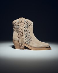 Botas vaqueras de ante beige con flecos decorativos, adornadas con tachuelas plateadas y detalles en turquesa. Diseño de punta redondeada y tacón apilado.